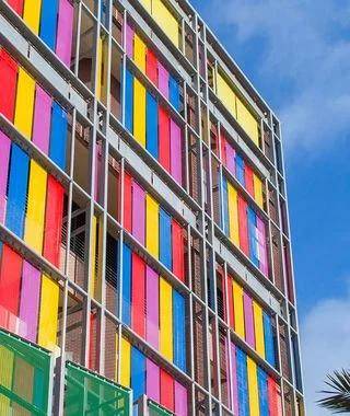 Colourful wire mesh façade consisting of yellow, blue, red and pink painted stainless steel meshes.