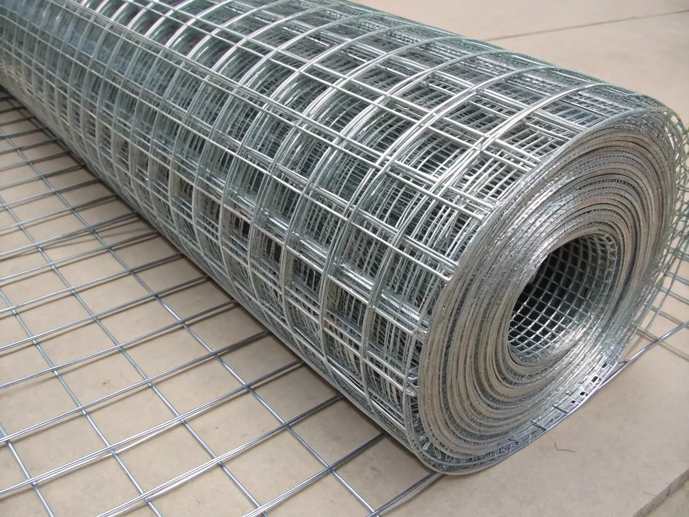 Galvanized steel wire mesh rolls with a shiny zinc coating, stored in an industrial setting.